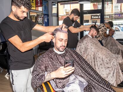 En primer plano Hamza Khmiessi, mirando su móvil mientras le cortan el pelo en MohaBarberStar, en el centro de Parla, un viernes por la tarde reciente antes de una primera cita con una chica.