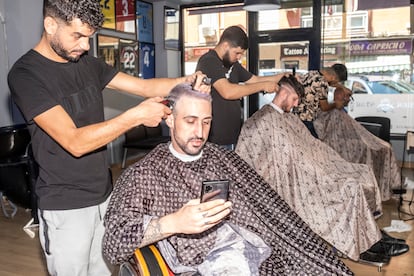 En primer plano Hamza Khmiessi, mirando su móvil mientras le cortan el pelo en MohaBarberStar, en el centro de Parla, un viernes por la tarde reciente antes de una primera cita con una chica.