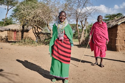 Runi Mukanda is one of the first chiefs who the PWC approached to try to improve the lives of women in the community. He is pictured in the background. Ahead of him, his wife, Ngoije, poses in the courtyard of their property, on June 5, 2024. 