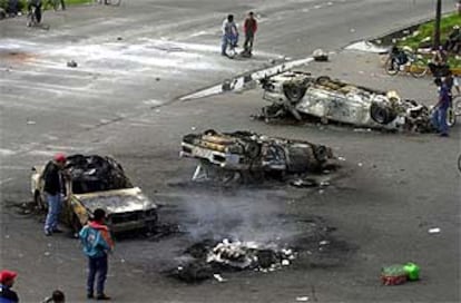 Campesinos de San Salvador Atenco bloquean una carretera junto a varios coches de policía quemados.