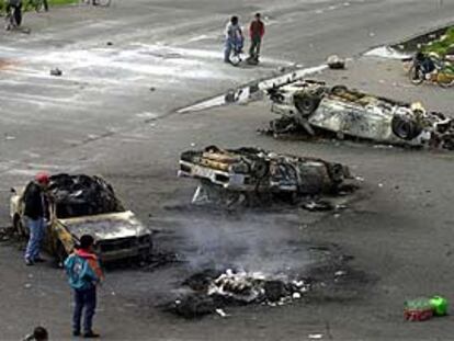 Campesinos de San Salvador Atenco bloquean una carretera junto a varios coches de policía quemados.