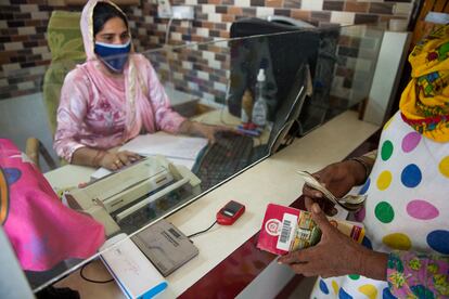 Una agente comercial ayuda a una mujer a realizar una transacción bancaria en Silana, India.