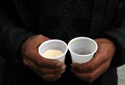 Una persona sin hogar sostiene un vaso de caldo y otro de cafe, ofrecido por Solidarios, en el centro de Madrid.