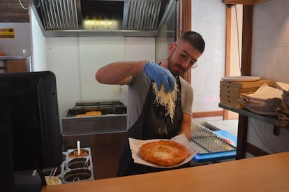 Un cocinero dispone sobre la masa abundante queso rallado de un lángos tradicional.