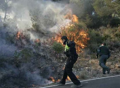 Varios agentes de policía tratan de sofocar el incendio declarado en Oropesa. La provincia de Castellón sufre desde anoche cinco incendios forestales avivados por las rachas de viento