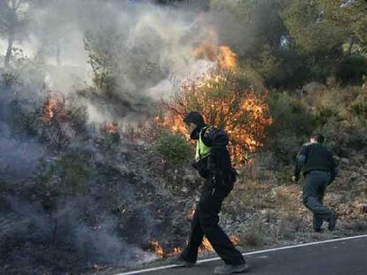 Varios agentes de policía tratan de sofocar el incendio declarado en Oropesa. La provincia de Castellón sufre desde anoche cinco incendios forestales avivados por las rachas de viento