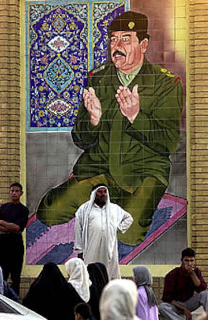 Varios iraquíes pasan junto a un cartel de Sadam Husein, en Bagdad. PLANO GENERAL - ESCENA