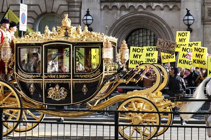 El rey  Carlos III y la reina Camila, pasan por delante de decenas de manifestantes antimonárquicos que levantan pancartas con el lema "No mi rey".