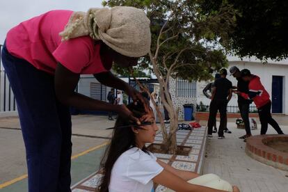 Una mujer subsahariana hace trenzas en el pelo a una niña melillense en la puerta del CETI de Melilla este miércoles.