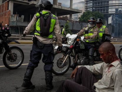 Homem ferido junto a policiais da Guarda Nacional Bolivariana.