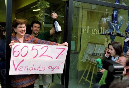 Dolores Lillo, dueña de la administración de lotería 'El Gallo de Oro', de Oviedo, muestra un cartel con el número 60.527, primer premio del sorteo del Niño que repartió el establecimiento íntegramente.