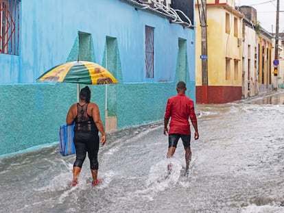 Dos personas caminan bajo la lluvia en una calle de Santiago de Cuba.