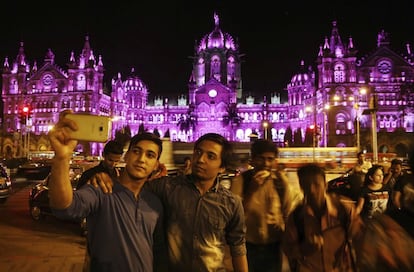 Un grupo de personas se fotografía delante de la estación Chhatrapati Shivaji Terminus, iluminada en color rosa como símbolo del Día de la Mujer en Bombay (India).
