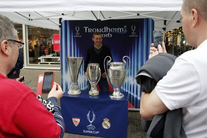 Un aficionado se fotografía con las copas de la Champions League, la Europa League y la Supercopa de Europa, que hoy se disputa en la localidad noruega de Trondheim entre el Real Madrid y el Sevilla FC.