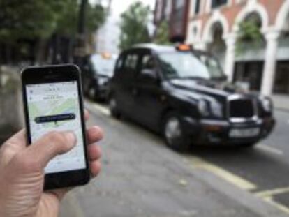 Un usuario utiliza la aplicaci&oacute;n de Uber frente a una parada de taxis de Londres. 