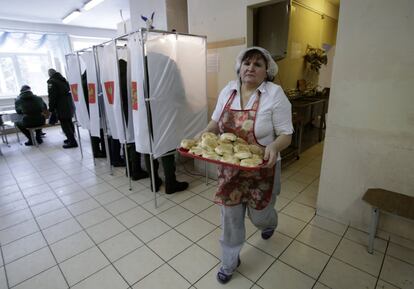 Una mujer lleva una bandeja llena de panecillos mientras la gente vota en un centro electoral de San Petersburgo (Rusia).