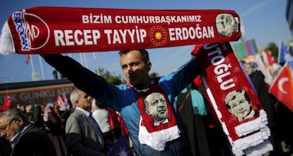 Un hombre sujeta banderas con la imagen y los nombres del presidente turco, Recep Tayyip Erdogan, y el primer ministro, Ahmet Davutoglu, mientras espera la llegada de este &uacute;ltimo al aeropuerto de Estambul, este martes.