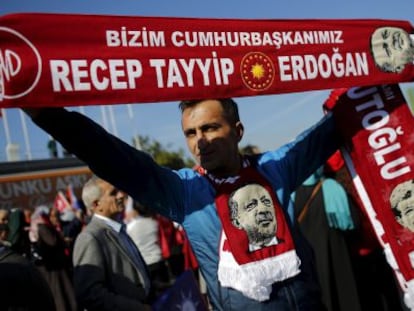 Un hombre sujeta banderas con la imagen y los nombres del presidente turco, Recep Tayyip Erdogan, y el primer ministro, Ahmet Davutoglu, mientras espera la llegada de este &uacute;ltimo al aeropuerto de Estambul, este martes.