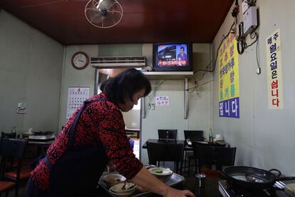 Una mujer recoge los platos mientras la televisión informa sobre el desfile por el 105 aniversario del fundador Kim Il-Sung.
