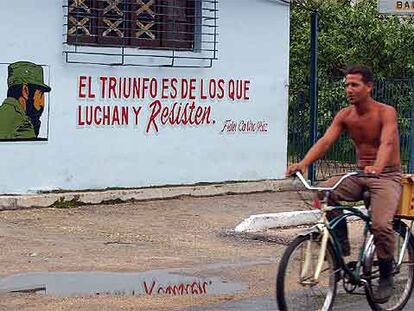 Un cubano pasa en bicicleta junto a un cartel con una consigna y la imagen de Fidel Castro en La Habana.