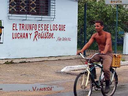 Un cubano pasa en bicicleta junto a un cartel con una consigna y la imagen de Fidel Castro en La Habana.