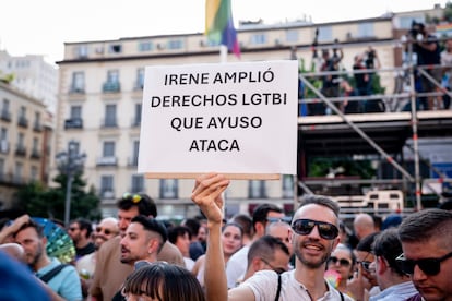 Un asistente al pregón del Orgullo de Madrid con una pancarta criticando el intento de Isabel Díaz Ayuso de recortar leyes LGTBI+ en la región. 