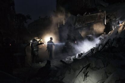 Milicianos sirios buscan supervivientes entre los escombros del edificio golpeado.