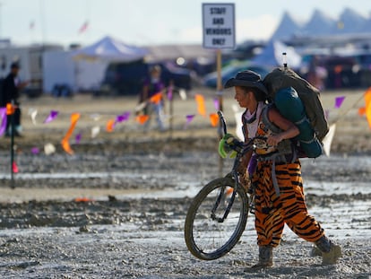 Un participante en el festival Burning Man lleva a pulso su bicicleta a través del barro tras la tormenta que dejó atrapadas a decenas de miles de asistentes.