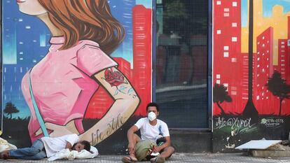 Dos sin techo descansan frente a un mural, en Sao Paulo.
