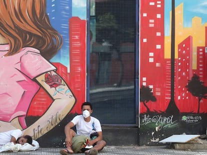 Dos sin techo descansan frente a un mural, en Sao Paulo.