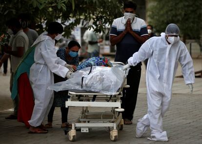 Dos personas se despiden de un familiar fallecido por el coronavirus mientras un trabajador sanitario tira de la camilla hacia un depósito de cadáveres, en Ahmedabad (India).