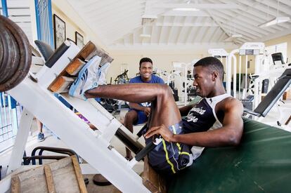 Waseem Williams, de 18 años y estrella velocista del Jamaica College, entrena sus piernas en la sala de máquinas del Jamaica College. Contempla sus ejercicios el destacado saltador Clayton Brown.