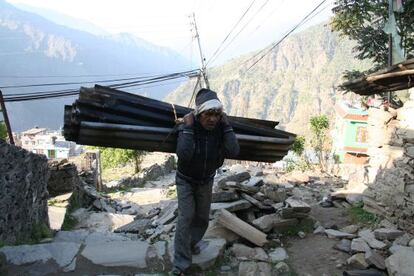 Un anciano carga con unas planchas de chapa para hacer el tejado de su casa en Dunche.