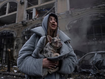 Ivanna calienta a su perro, frente a un automóvil destruido en llamas después de un reciente ataque ruso en Kiev (Ucrania).
