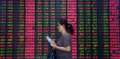 Una mujer camina en Shanghai frente a un panel de datos bancarios