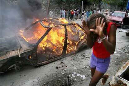 Una niña corre cerca de un coche quemado por los seguidores del candidato René Préval ayer en Puerto Príncipe.