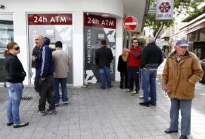 Un grupo de personas hace cola junto al cajero automático de una sucursal cerrada del banco Laiki, en Nicosia. El Parlamento chipriota se reúne esta mañana para debatir y previsiblemente votar el plan elaborado por el Gobierno como alternativa a las propuestas del Eurogrupo, mientras que el tiempo apremia por temor a una bancarrota desordenada.