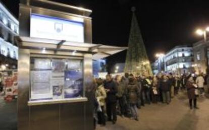 Cola frente a una administración de lotería de la madrileña Puerta del Sol, con el árbol patrocinado por Loterías y Apuestas del Estado al fondo