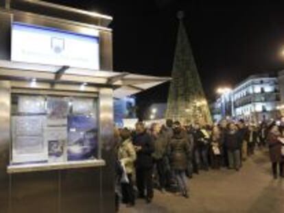 Cola frente a una administraci&oacute;n de loter&iacute;a de la madrile&ntilde;a Puerta del Sol, con el &aacute;rbol patrocinado por Loter&iacute;as y Apuestas del Estado al fondo