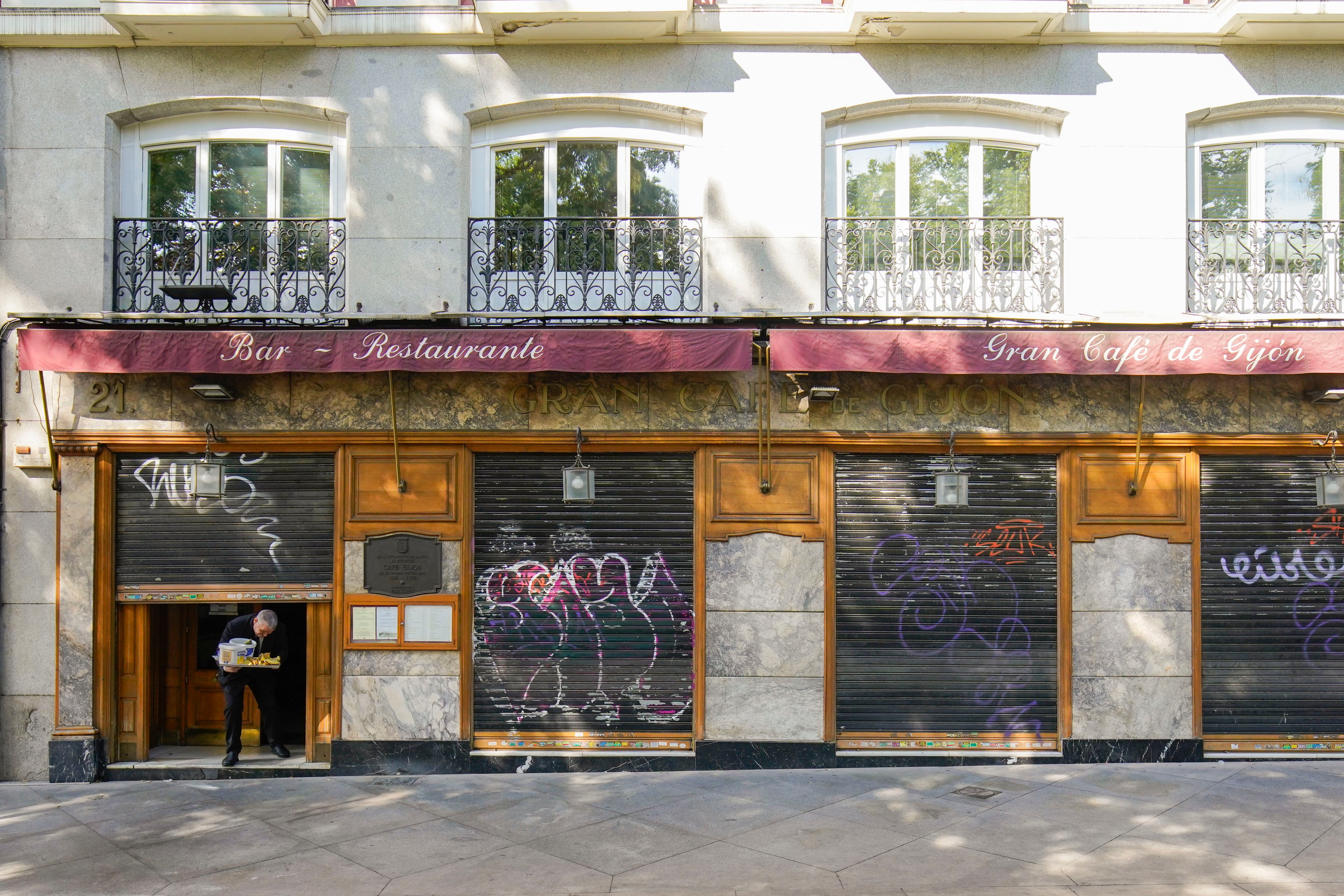 Un trabajador pasa por debajo de la puerta de la entrada medio cerrada del Gran Café Gijón en Madrid, este viernes.