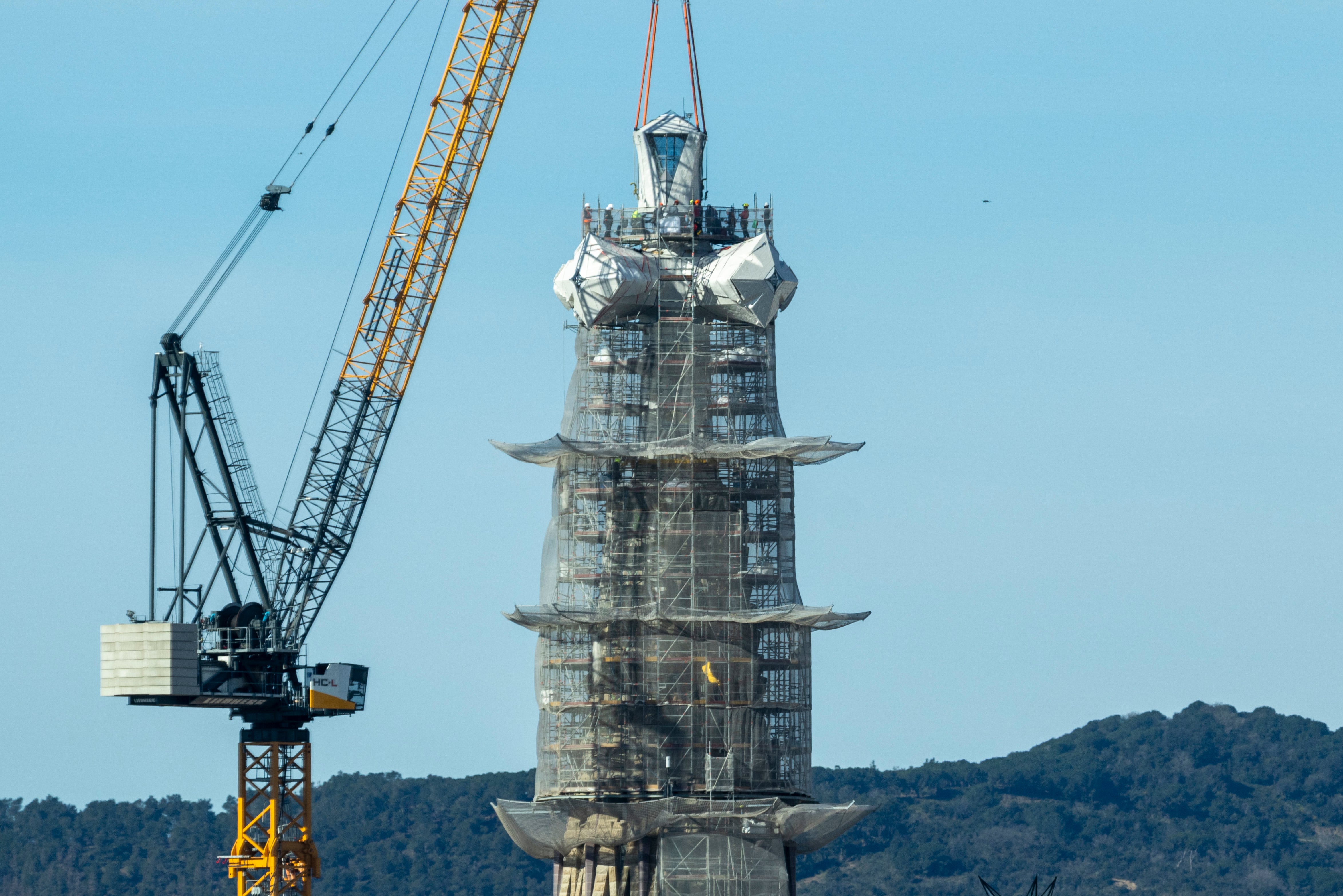 La grúa y una docena de operarios, el día 20 de febrero, trabajando en la colocación de la última pieza de la cruz que corona la torre de Jesucristo de la Sagrada Familia de Barcelona. Desde ese día se ha retirado el andamio que cubría el tramo final de la torre más alta.