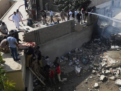 Varios voluntarios retiran el cuerpo sin vida de uno de los pasajeros que iban a bordo del avión estrellado en Karachi (Pakistán), este viernes.