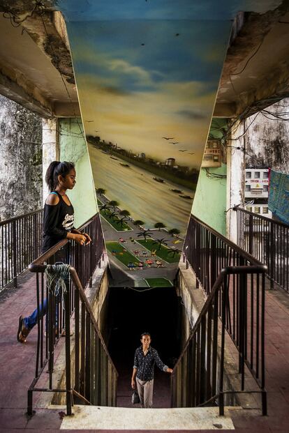 Existe un edificio blanco que se cae pedazos, decrépito y situado en pleno centro de una Phnom Penh -la capital de Camboya- en rápido cambio. Parece ajeno a los rascacielos de vidrio y acero que brotan a su alrededor. Pero la pujante comunidad formada por más de 2.500 artistas, monjas, trabajadoras del sexo y empleados públicos que vive en este enorme asentamiento marginal saben muy bien que lo que para ellos es su hogar tiene las horas contadas. En la imagen, un mural en la escalera con una representación de Phnom Penh y el río Mekong.