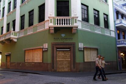 Una pareja camina frente a una tienda ya protegida con tablones ante la amenaza del huracán María en Puerto Rico, donde pesa una alerta roja ya que se trata de "una tormenta capaz de poner en peligro vidas humanas" con intenso oleaje, subidas repentinas del nivel del mar, deslaves e intensas lluvias.