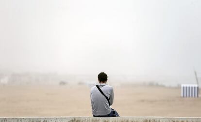Un joven contempla la playa de la Malvarrosa cubierta por la niebla que ha obligado a cerrar el puerto de valencia al tráfico marítimo.