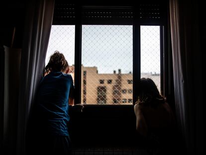 Dos niñas miran por la ventana de su casa, durante el confinamiento por la pandemia del coronavirus.