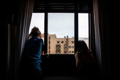 Dos niñas miran por la ventana de su casa, durante el confinamiento por la pandemia del coronavirus.