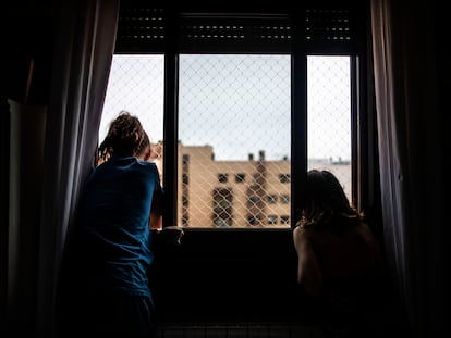 Dos niñas miran por la ventana de su casa, durante el confinamiento por la pandemia del coronavirus.