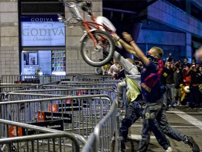 Dos alborotadores lanzando una bicicleta por encima de las vallas dipuestas por la policía para limitar las agresiones.