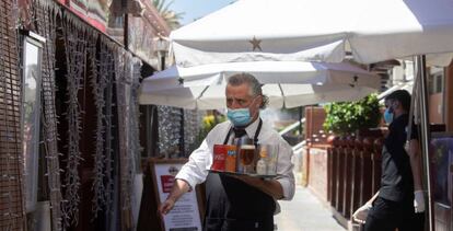 Un camarero lleva su pedido a unos clientes a una de las terrazas del Puerto Olímpico de Barcelona, este miércoles, cuando la ciudad entra en su tercer día en la fase 1 de la desescalada.